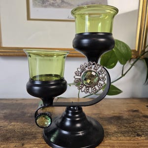 Peut inclure: Un bougeoir en métal noir doté de deux coupelles en verre vert citron à des hauteurs différentes. La structure est ornée de deux décorations circulaires en filigrane argenté, chacune centrée par une gemme en verre vert citron facetté.