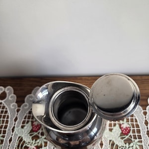 Puede incluir: Una taza de cer&aacute;mica blanca con un asa negra y el texto "But First, Coffee" en negro, con una fuente de estilo manuscrito. La taza est&aacute; sobre una superficie blanca.