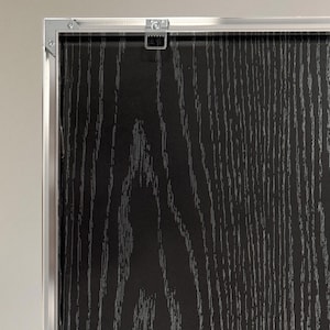 Puede incluir: Primer plano de un panel enmarcado con vetas de madera en negro y gris. El marco es de metal plateado. Un colgador de metal est&aacute; fijado en la parte superior del marco.