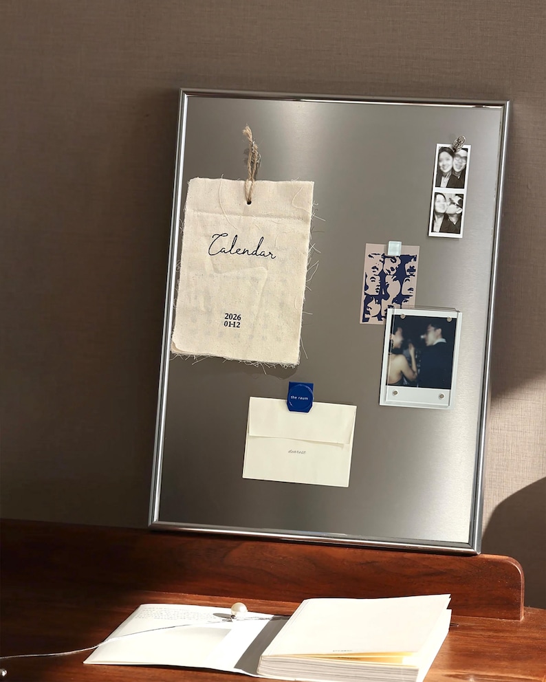 Puede incluir: Un tablero magn&eacute;tico con marco plateado que muestra un calendario de tela, fotos y notas. El calendario es de tela texturizada blanquecina con la palabra "Calendar" y la fecha "2026 01-12" impresas. Otros elementos se adjuntan con imanes.