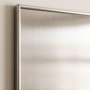 Puede incluir: Primer plano de un panel de acero inoxidable cepillado con un marco met&aacute;lico delgado. La superficie tiene un patr&oacute;n de vetas verticales, que refleja la luz. El marco tiene un borde redondeado. El panel est&aacute; montado en una pared de color claro.