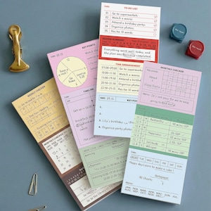 Może przedstawiać: Biały ceramiczny kubek z czarnym uchwytem i napisem "But First, Coffee" w stylu odręcznym. Kubek stoi na białej powierzchni. Kubek ma około 10 cm wysokości.