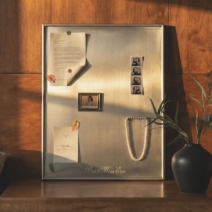 May include: A white ceramic mug with a black handle and the text "But First, Coffee" in a bold, black font. The mug is set against a blurred background, suggesting a cosy setting.