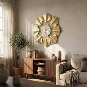 Può includere: Un grande orologio da parete in metallo dorato con un design floreale. L'orologio ha un quadrante bianco con numeri e lancette nere. L'orologio è montato su una parete di colore neutro sopra un mobile in legno.