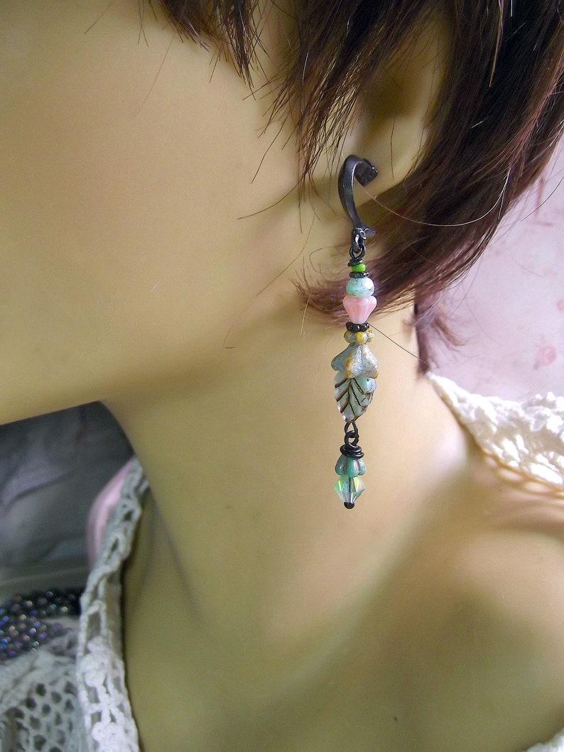May include: A silver leaf dangle earring with a black wire wrapped around the top and a crystal bead at the bottom. The earring is accented with pink, green, and blue beads.