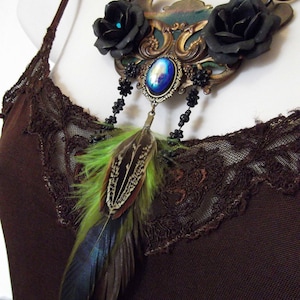 May include: A black and green feather necklace with a large ornate metal pendant featuring black roses and a blue iridescent stone.