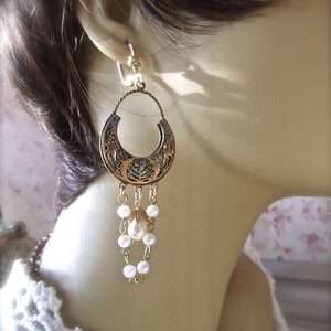 Puede incluir: Pendientes de tono dorado con un gran dise&ntilde;o circular adornado y una perla colgante. Los pendientes est&aacute;n en un maniqu&iacute; blanco.