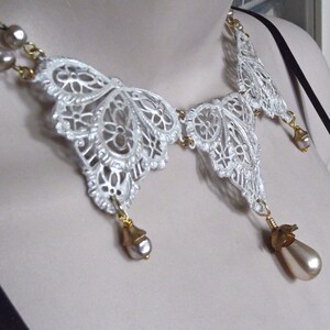 May include: A white lace butterfly necklace with gold accents and pearl drops. The necklace is delicate and feminine, and would make a beautiful gift for a special occasion.