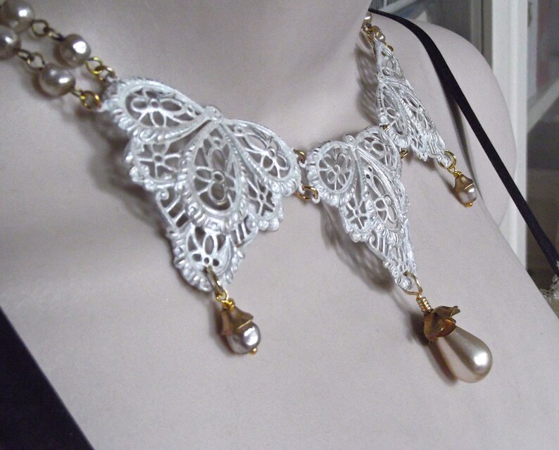 May include: A white lace butterfly necklace with gold accents and pearl drops. The necklace is delicate and feminine, and would make a beautiful gift for a special occasion.