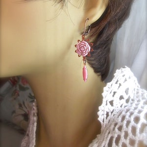 May include: A pair of pink rose earrings with a copper finish. The earrings feature a delicate pink rose charm with a copper wire design and a dangling pink teardrop charm.