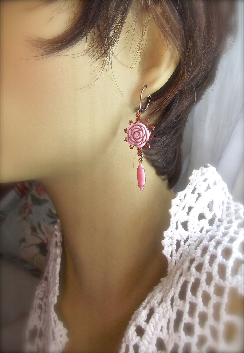 May include: A pair of pink rose earrings with a copper finish. The earrings feature a delicate pink rose charm with a copper wire design and a dangling pink teardrop charm.