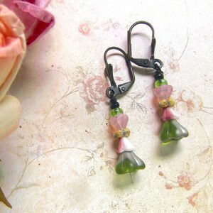 May include: A pair of dangle earrings with green, pink, and white glass beads. The earrings have a black metal hook.