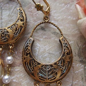 Puede incluir: Un par de pendientes de tono dorado con un dise&ntilde;o de media luna y detalles de perlas colgantes. Los pendientes tienen un cierre de gancho.