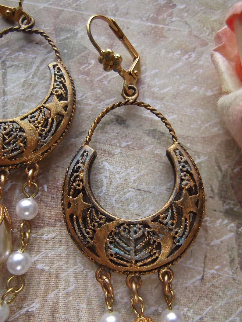 Puede incluir: Un par de pendientes de tono dorado con un dise&ntilde;o de media luna y detalles de perlas colgantes. Los pendientes tienen un cierre de gancho.
