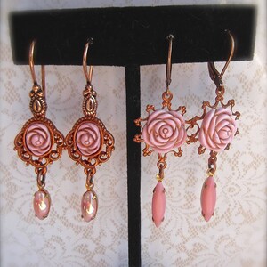 May include: A pair of pink rose dangle earrings with copper-toned metal accents. The earrings feature a delicate rose design with a pink glass center and a dangling pink glass teardrop.