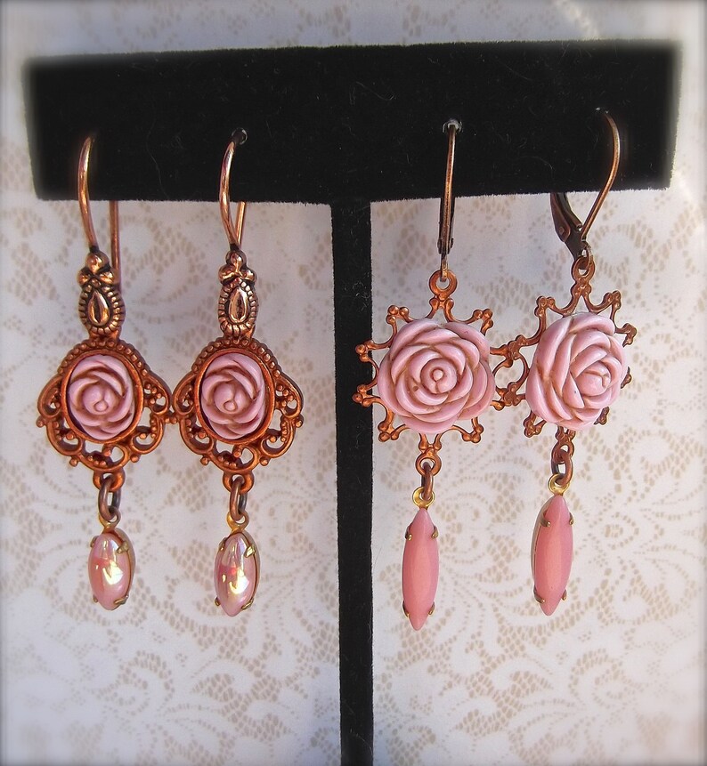 May include: A pair of pink rose dangle earrings with copper-toned metal accents. The earrings feature a delicate rose design with a pink glass center and a dangling pink glass teardrop.