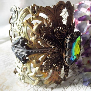 May include: A gold and silver ornate bracelet with a large iridescent green gemstone. The bracelet is made of metal and has a delicate, intricate design.
