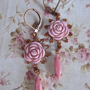 May include: A pair of copper earrings with pink rose-shaped charms and pink teardrop-shaped dangles.