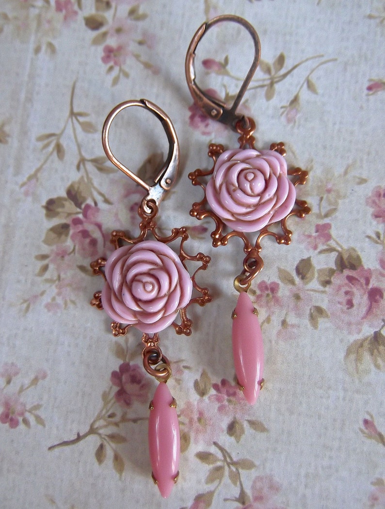 May include: A pair of copper earrings with pink rose-shaped charms and pink teardrop-shaped dangles.