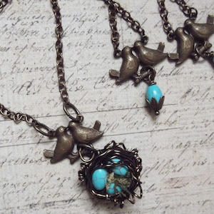 May include: A bronze necklace with a bird and nest pendant. The nest is filled with turquoise blue stones. The necklace has a chain with two bird charms and turquoise blue stones.