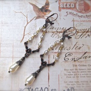 May include: A pair of dangle earrings with a vintage style. The earrings feature a delicate chain with small white pearls and a bronze floral design. The earrings have a teardrop-shaped pearl at the bottom.