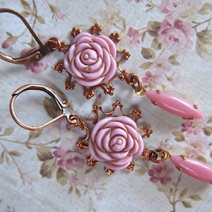 May include: A pair of pink rose earrings with copper-toned metal accents. The earrings feature a delicate floral design and are perfect for adding a touch of vintage charm to any outfit.