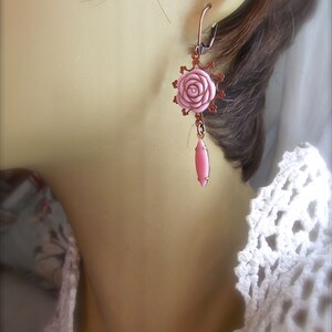 May include: A pair of pink rose earrings with a dangling pink teardrop charm. The earrings are made of copper and have a delicate, feminine design.