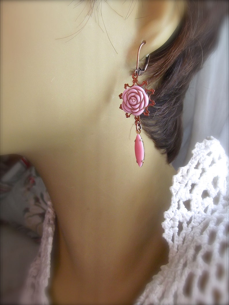 May include: A pair of pink rose earrings with a dangling pink teardrop charm. The earrings are made of copper and have a delicate, feminine design.