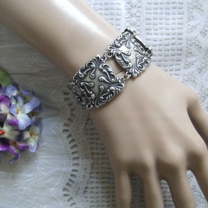 May include: A silver bracelet with a decorative design of interlocking squares and swirls.