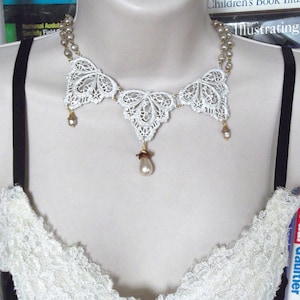 May include: A white lace necklace with a butterfly design and pearl accents. The necklace is on a white background.