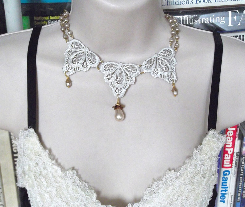 May include: A white lace necklace with a butterfly design and pearl accents. The necklace is on a white background.
