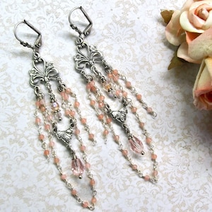 May include: Silver tone dangle earrings with multiple strands of delicate chains and pink beads. The earrings feature a floral design at the top.