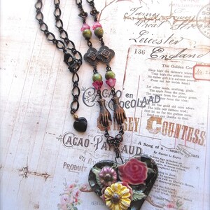 Pode incluir: Um colar com um pingente em forma de cora&ccedil;&atilde;o preto com um design floral. O pingente &eacute; feito de cer&acirc;mica e apresenta flores rosa, amarelas e verdes. O colar &eacute; feito de corrente de metal preto com contas verdes e rosas.