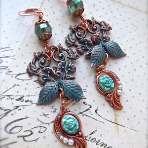 May include: A pair of long, dangling earrings with a copper and turquoise colour scheme. The earrings feature a delicate floral design with leaves and a small turquoise flower at the bottom.