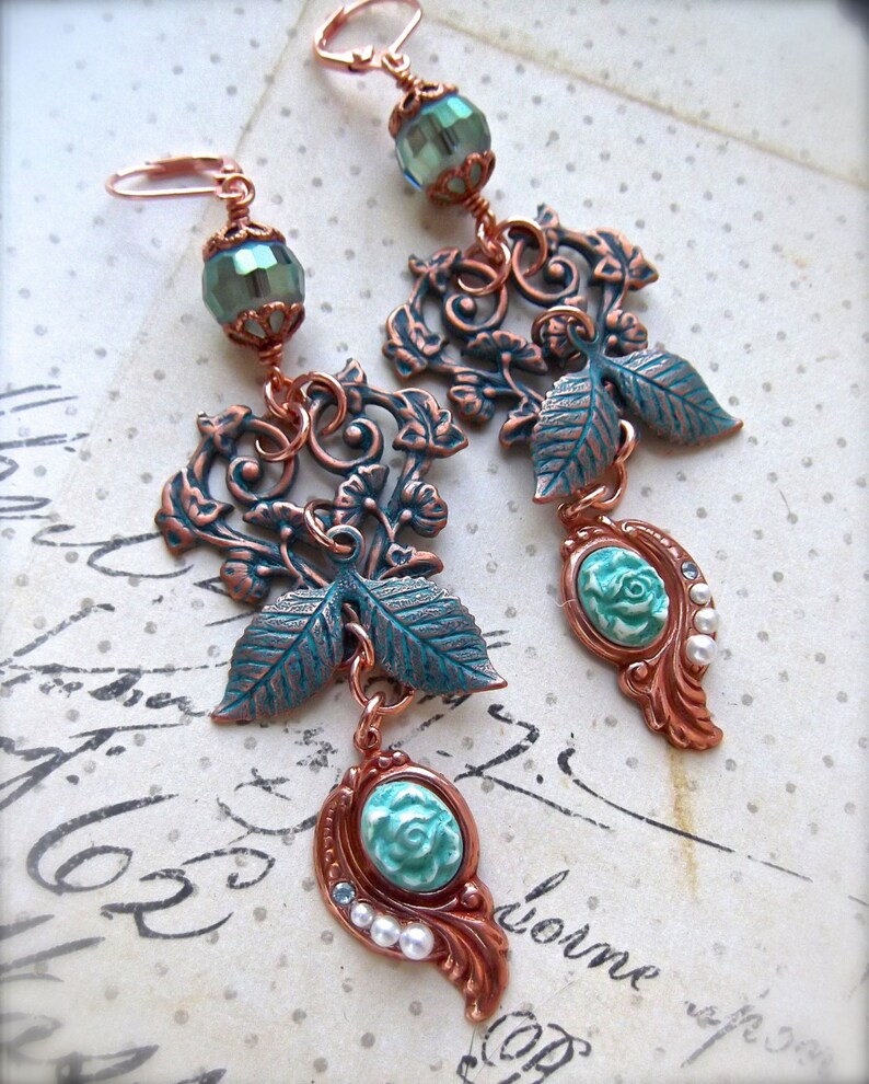 May include: A pair of long, dangling earrings with a copper and turquoise colour scheme. The earrings feature a delicate floral design with leaves and a small turquoise flower at the bottom.