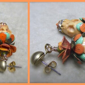 May include: A pair of skull-shaped earrings with colorful floral accents. The earrings are made of bone and feature a mix of turquoise, orange, and white colors. The earrings are attached to gold-toned ear wires.