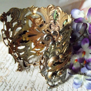 May include: A gold and silver ornate metal bracelet with a chain detail. The bracelet is intricately designed with floral patterns and has a vintage aesthetic.