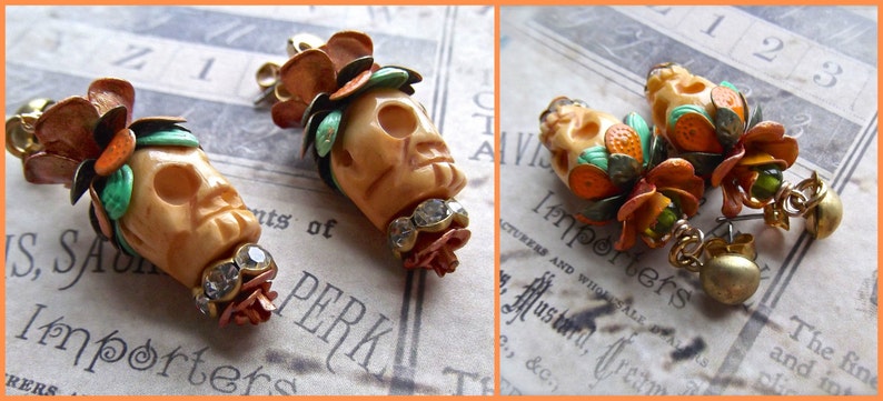 May include: A pair of skull-shaped earrings with orange, green, and white floral accents. The earrings are made of metal and have a vintage style.