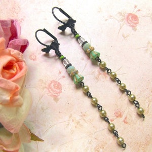 May include: A pair of long, dangling earrings with green and gold beads and black metal hooks.