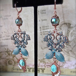 May include: A pair of copper filigree earrings with turquoise and white cameo accents. The earrings feature a leafy design with a heart-shaped centre.