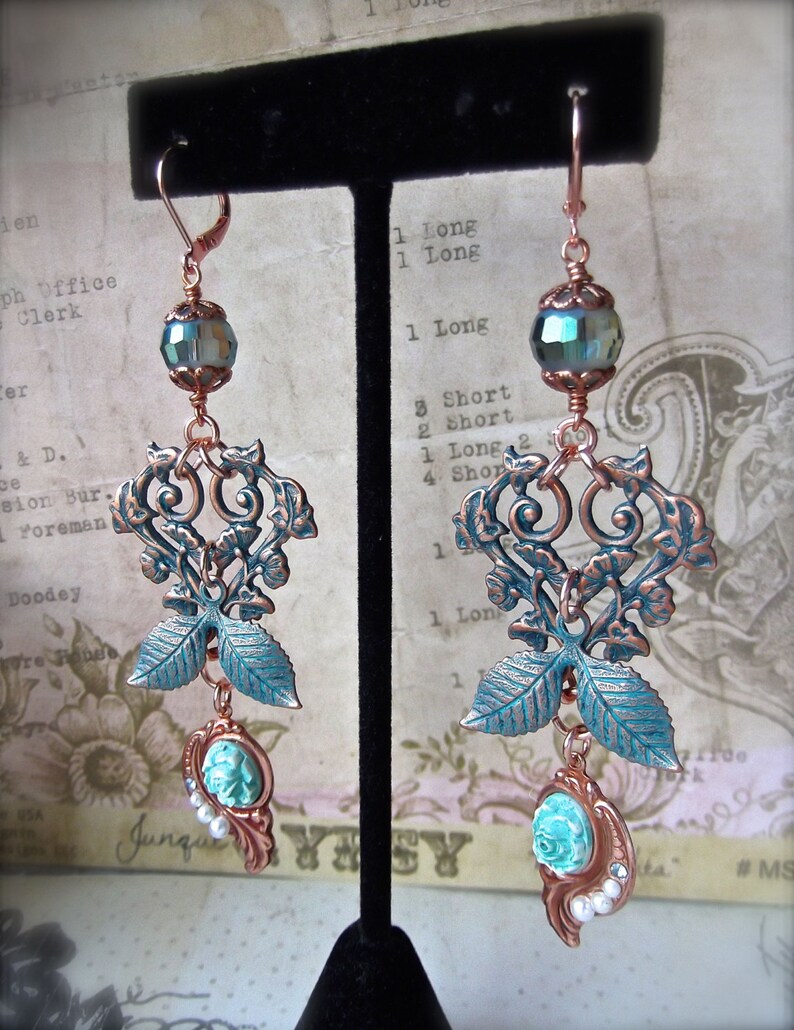May include: A pair of copper filigree earrings with turquoise and white cameo accents. The earrings feature a leafy design with a heart-shaped centre.