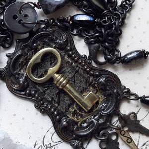 May include: A black and gold necklace with a large ornate key pendant, black buttons, and a chain with black beads.