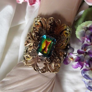 May include: A gold-toned metal cuff bracelet with an ornate design and a large, iridescent green gemstone in the center.