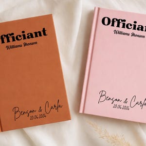 Puede incluir: Dos cuadernos de tapa dura, uno en naranja cálido y otro en rosa claro. La palabra "Officiant" está impresa en negrita negra en la parte superior, con un nombre debajo. La parte inferior de cada libro tiene los nombres de una pareja y una fecha.