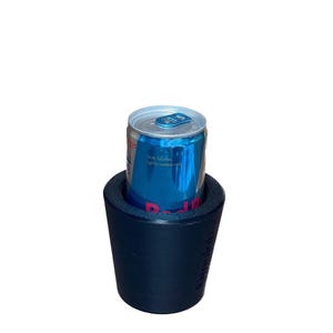 May include: A blue and silver Red Bull energy drink can inside a navy blue insulated beverage holder. The can has blue and silver text. The beverage holder has the text "kiinoolab" on the side.
