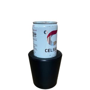 May include: A light blue Celsius energy drink can with red and silver accents, resting on a black, conical drink holder. The can features the text "CELSIUS LIVE" and "SUGAR - NO PRESERVATIVES".