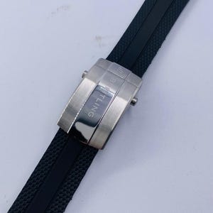 K&ouml;nnte beinhalten: Ein schwarzes Kautschuk-Uhrenarmband mit strukturierter Oberfl&auml;che und einer silberfarbenen Metall-Faltschlie&szlig;e. Die Schlie&szlig;e zeigt das eingravierte Breitling-Logo und den Markennamen auf ihrer geb&uuml;rsteten und polierten Oberfl&auml;che.