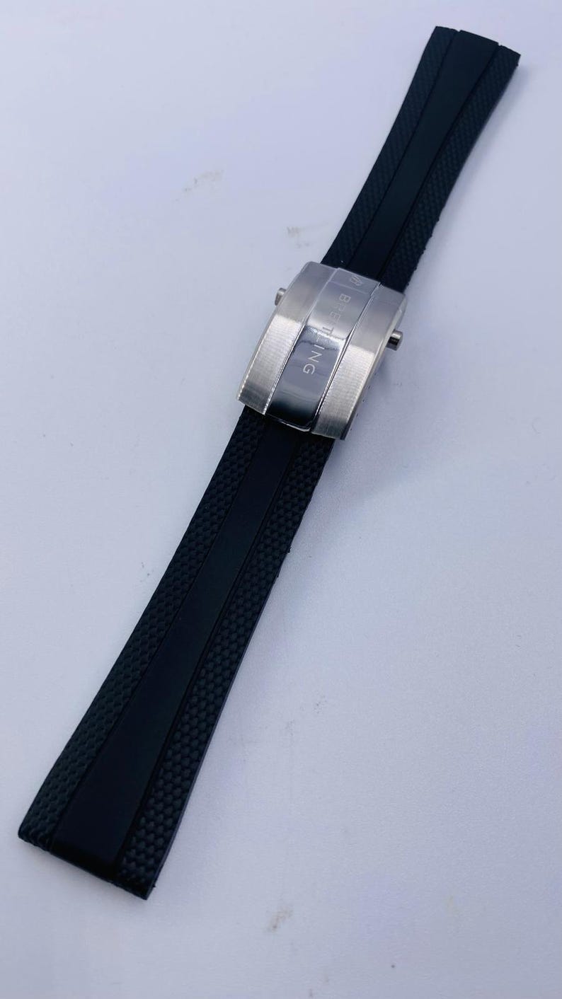 K&ouml;nnte beinhalten: Ein schwarzes Kautschuk-Uhrenarmband mit strukturierter Oberfl&auml;che und einer Faltschlie&szlig;e aus geb&uuml;rstetem Edelstahl. Die Schlie&szlig;e ist mit dem eingravierten Schriftzug BREITLING und einem kleinen Logo versehen, das einen sicheren Verschluss bietet.