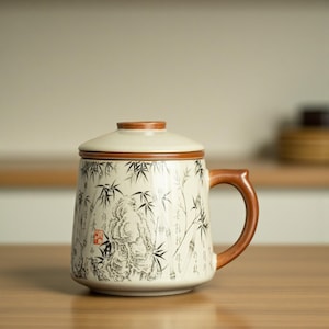 May include: A ceramic mug with a lid, brown handle and rim. The mug is decorated with a black and white bamboo forest design and a figure. The mug is likely used for tea or coffee.
