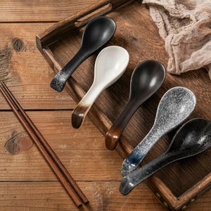 Może przedstawiać: Zestaw trzech ceramicznych kubków z nakrapianym, matowym wykończeniem. Kubki są w odcieniach kremu, jasnego brązu i ciemnego brązu. Każdy kubek ma prosty design i zaokrąglony uchwyt.